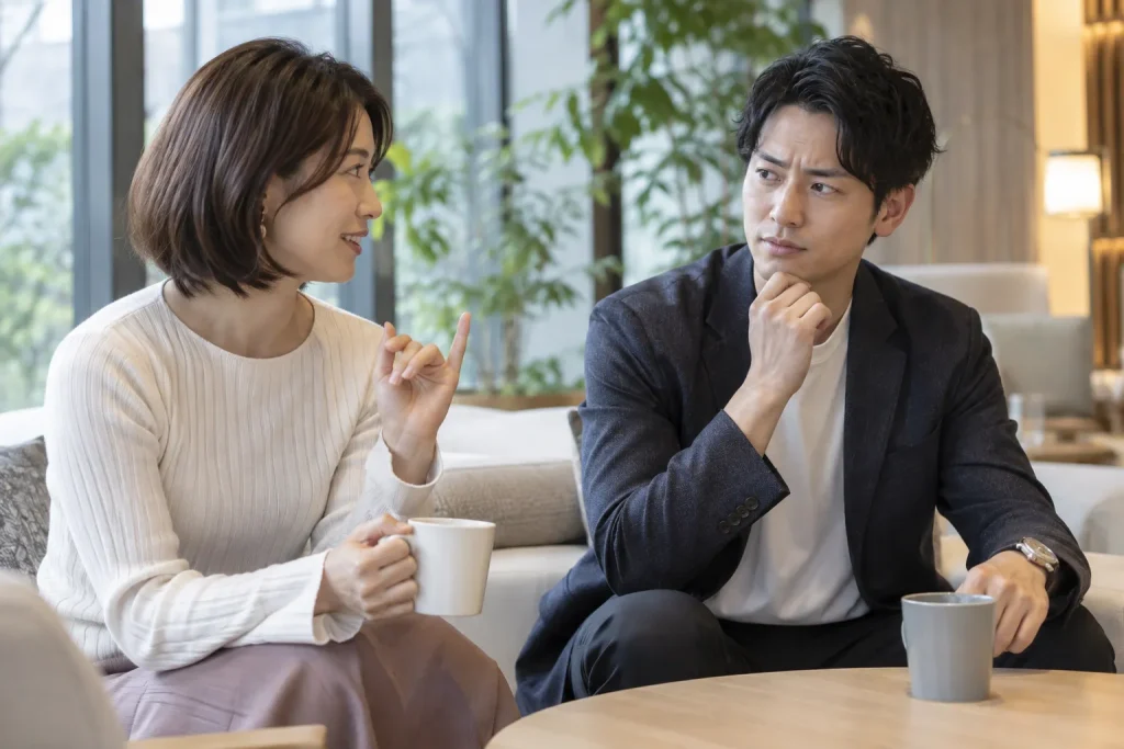 Two adult friends in casual conversation, with one discreetly raising a little finger while the other looks uncertain.